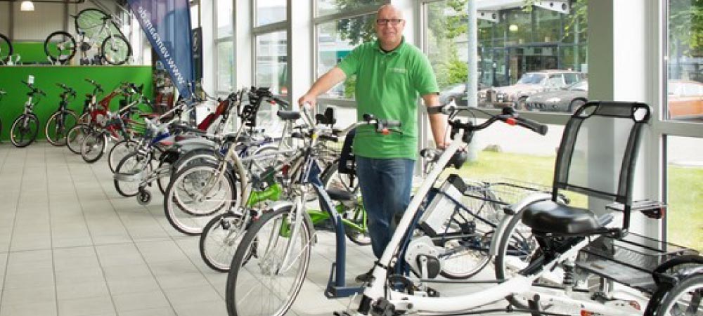 Ein Dreirad-Berater steht vor einer großen Auswahl an verschiedenen Dreirädern